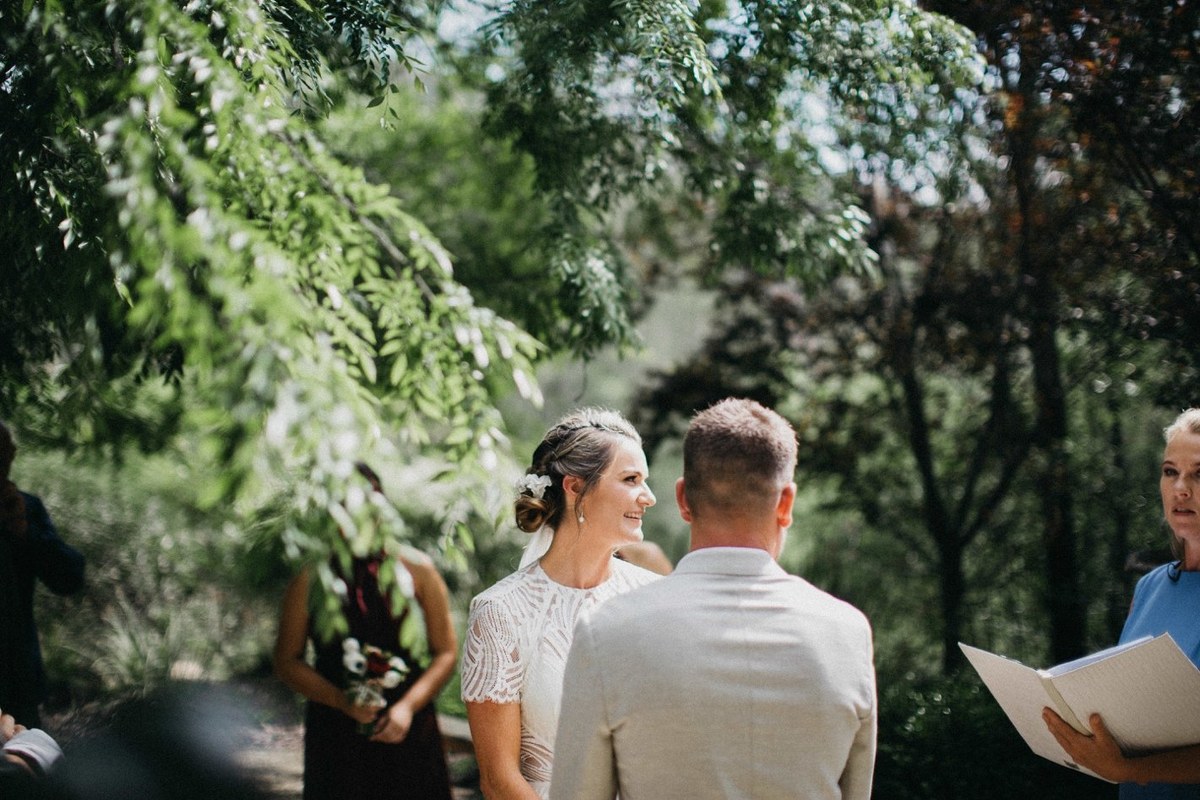 The bride walks down the aisle toward the ceremony beneath the trees. Photograph by documentary wedding photographer Joshua Mikhaiel.