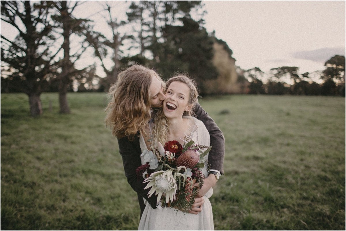 The bride laughs with a friend as they walk across the grass, photographed by documentary wedding photographer Joshua Mikhaiel.