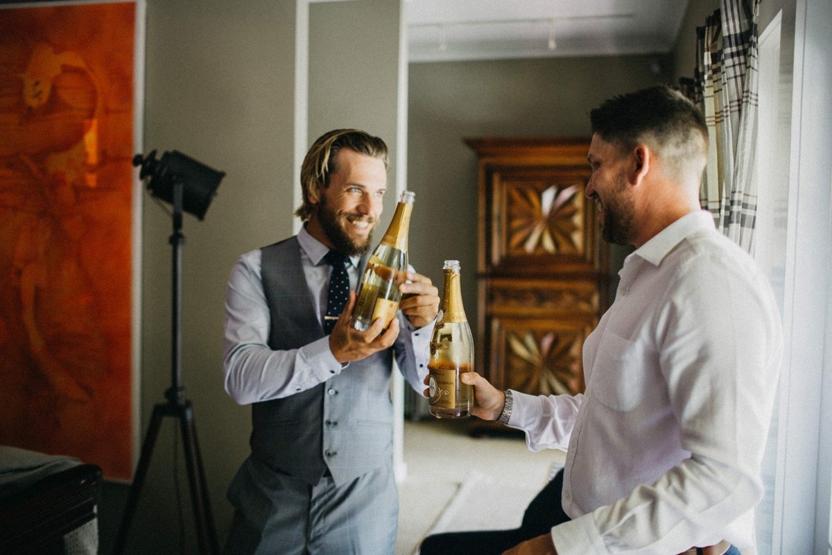 The groom inspects his suit while an attendant adjusts his boutonniere. Photograph by documentary wedding photographer Joshua Mikhaiel.