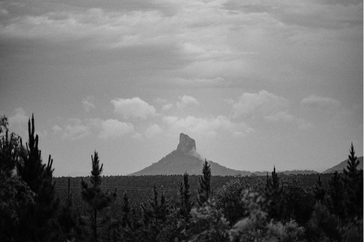 Glass House Mountains landscape — Joshua Mikhaiel, documentary wedding photographer A mountain rises above a line of trees in a black-and-white landscape. Photograph by documentary wedding photographer Joshua Mikhaiel.