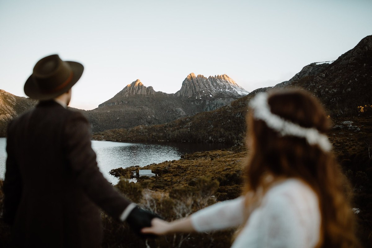 A couple stand beside an alpine lake with a jagged mountain range behind them, photographed by documentary wedding photographer Joshua Mikhaiel.