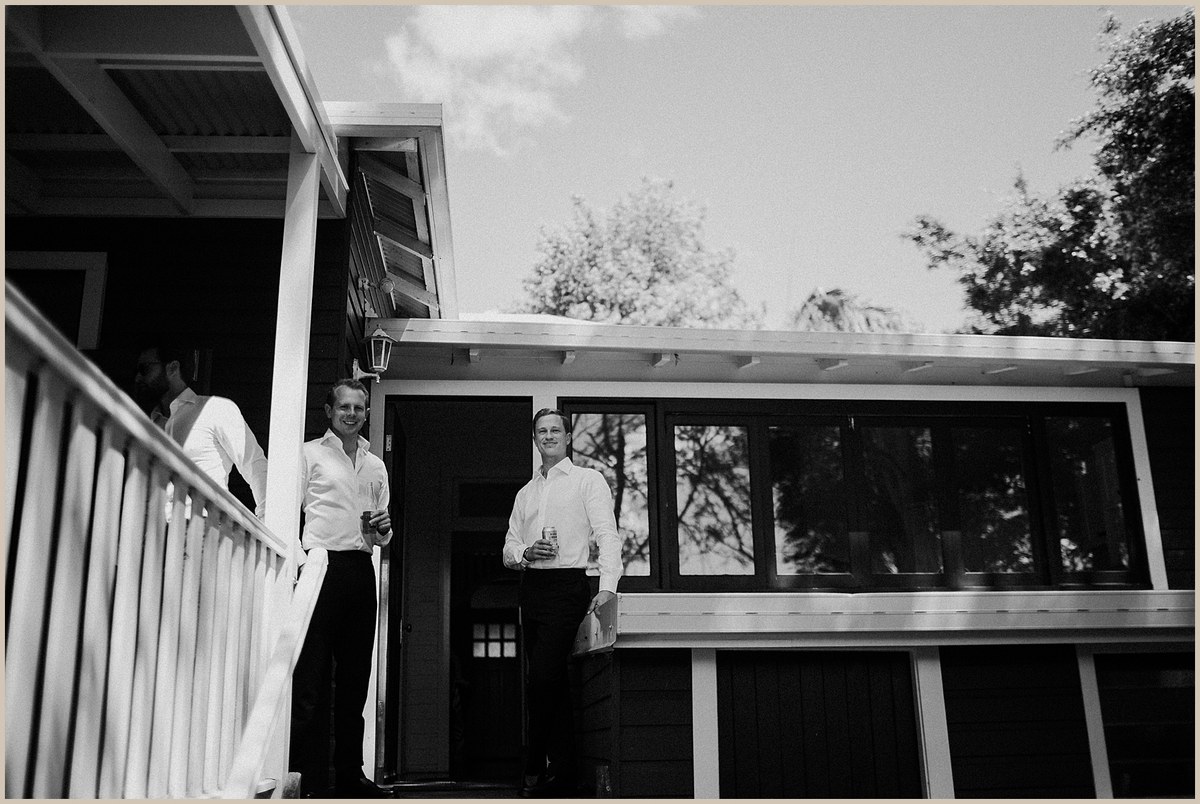 A black-and-white view shows a couple standing together on the veranda. Photograph by documentary wedding photographer Joshua Mikhaiel.