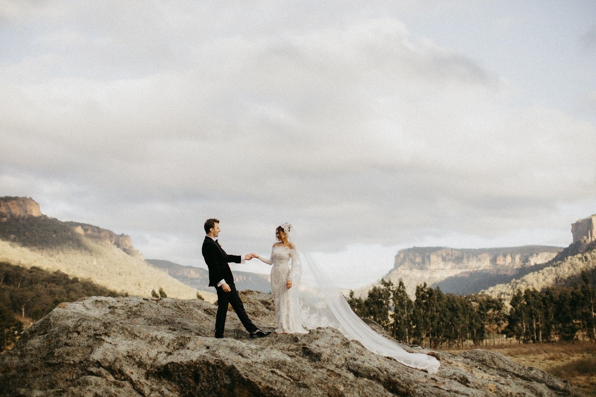 The bride and groom walk across a rocky ridge above a broad mountain valley. Photograph by documentary wedding photographer Joshua Mikhaiel.