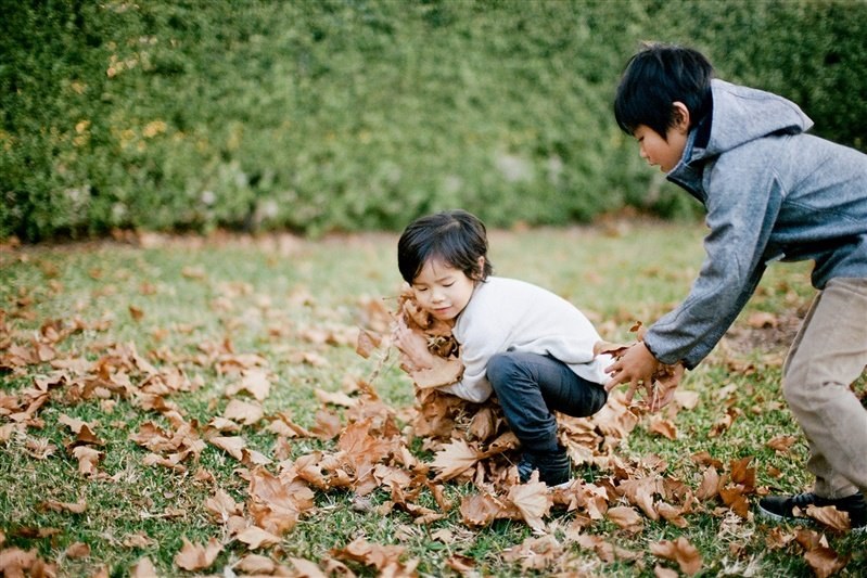 A father crouches beside his young daughter as she explores fallen leaves, photographed by documentary wedding photographer Joshua Mikhaiel.