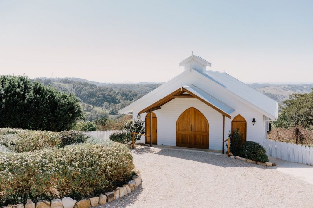 Summergrove Estate chapel exterior — Kirk Wilcox A small white chapel stands beside a landscaped garden and gravel drive.