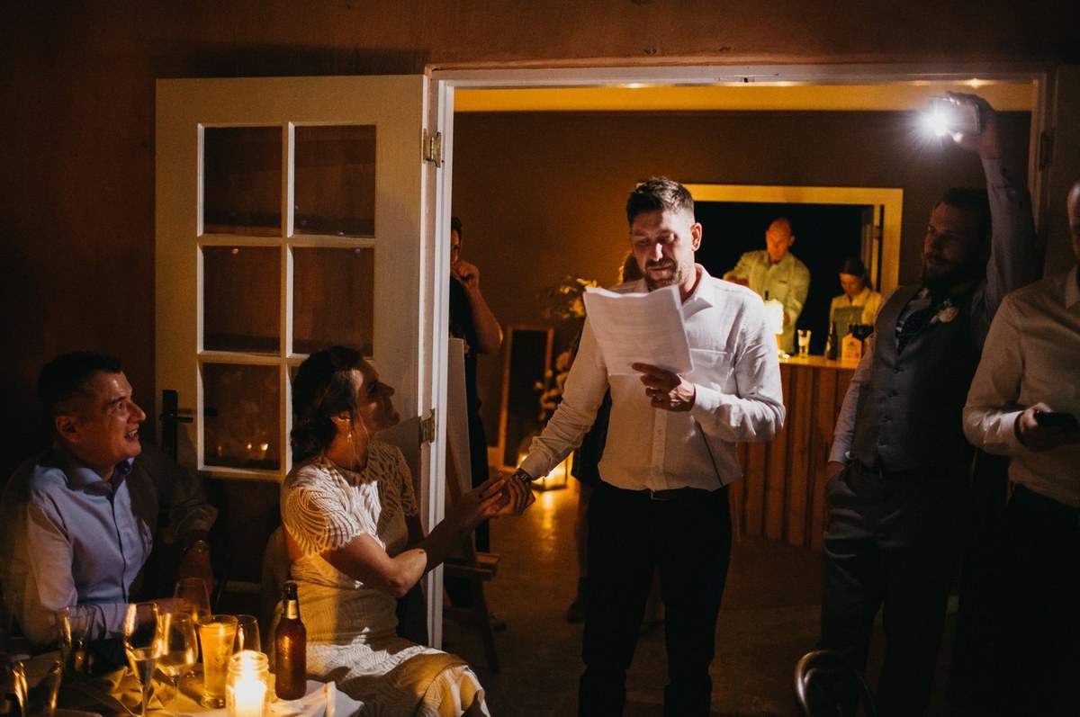 A man speaks into a microphone while guests watch. Photograph by documentary wedding photographer Joshua Mikhaiel.
