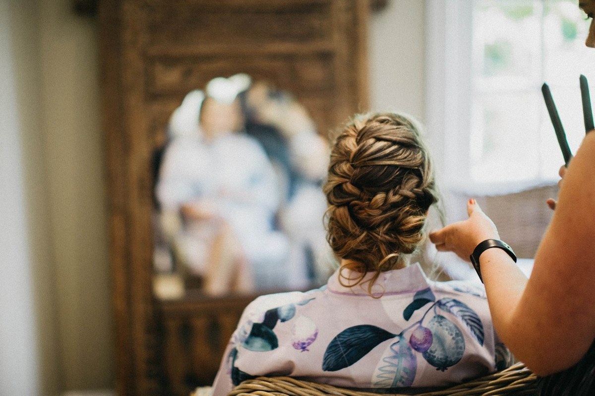 An attendant styles the bride’s hair as she sits before the mirror. Photograph by documentary wedding photographer Joshua Mikhaiel.