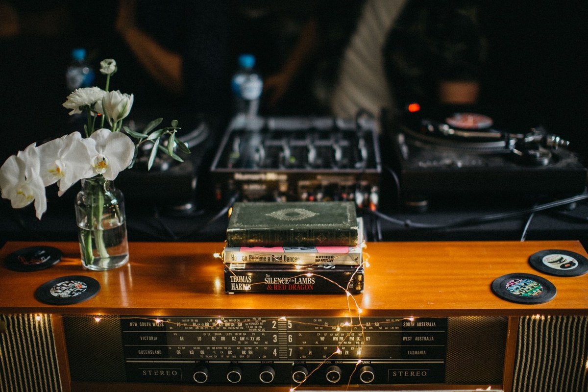 A DJ works behind a wooden booth with turntables and a laptop. Photograph by documentary wedding photographer Joshua Mikhaiel.