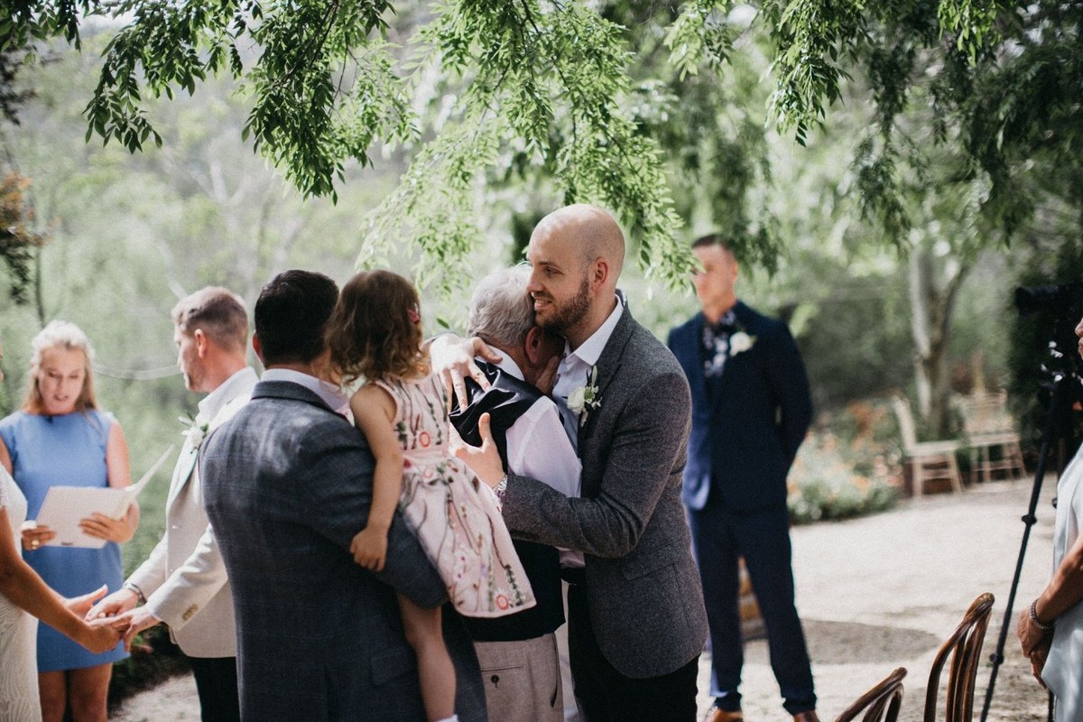 A guest embraces the bride beside the ceremony seating. Photograph by documentary wedding photographer Joshua Mikhaiel.