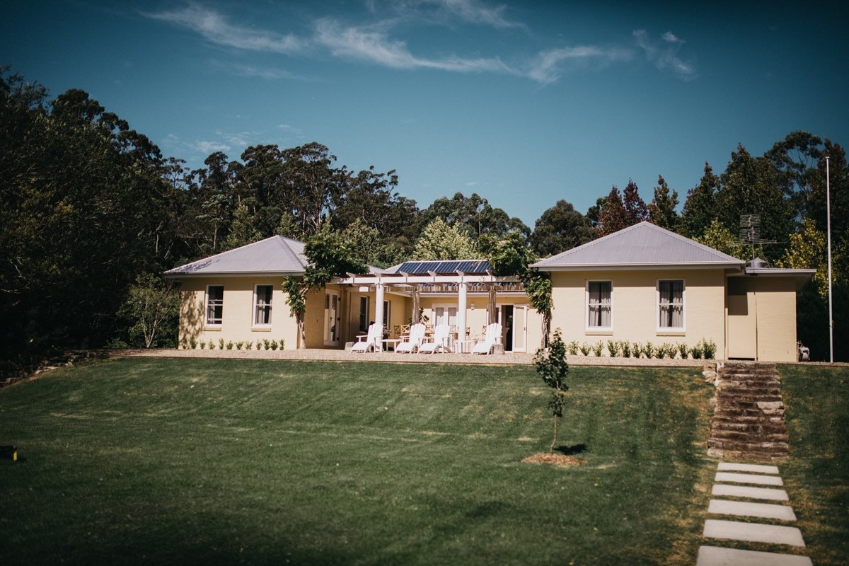 A country house sits beyond a broad green lawn and stone path, photographed by documentary wedding photographer Joshua Mikhaiel.