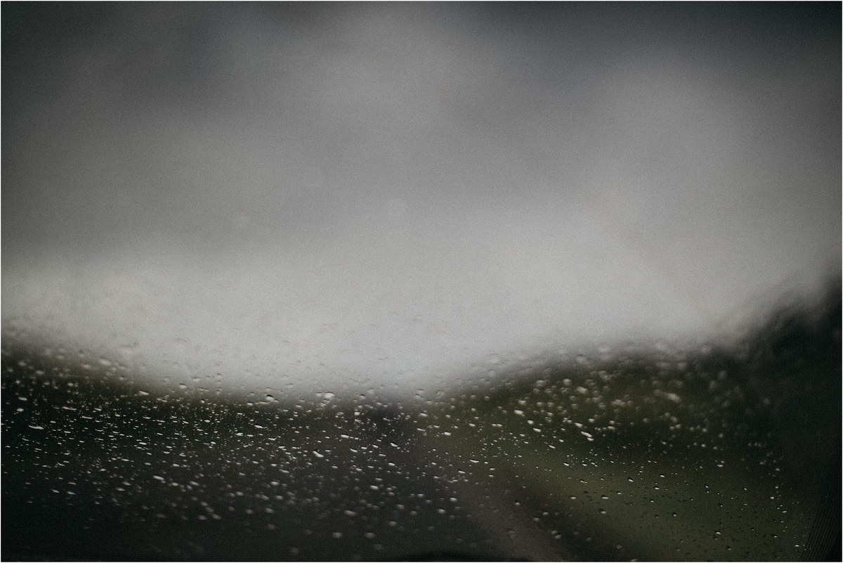 Rain beads on a window while the landscape outside fades into mist, photographed by documentary wedding photographer Joshua Mikhaiel.