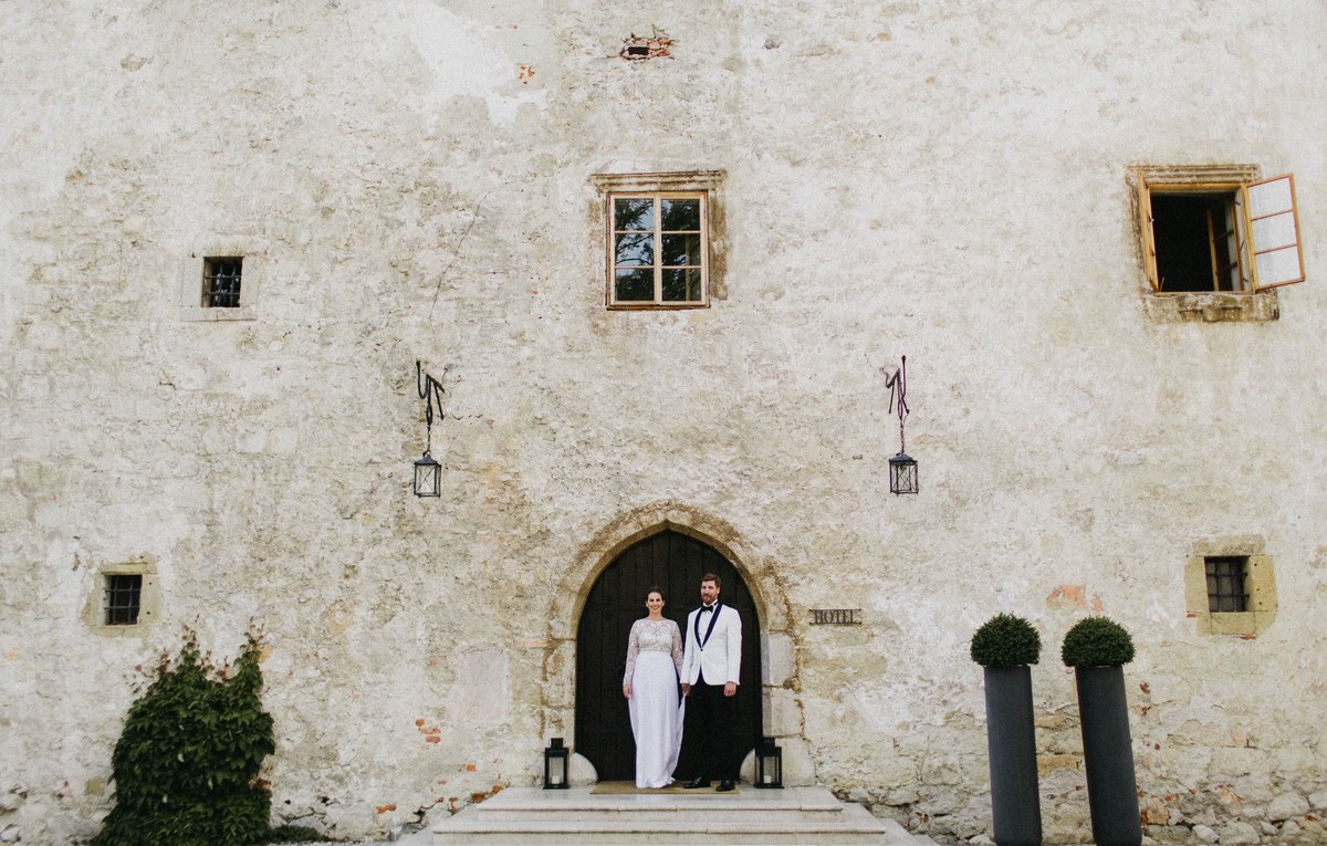 A wedding couple stand in an arched stone doorway beneath ivy-covered castle walls, photographed by documentary wedding photographer Joshua Mikhaiel.