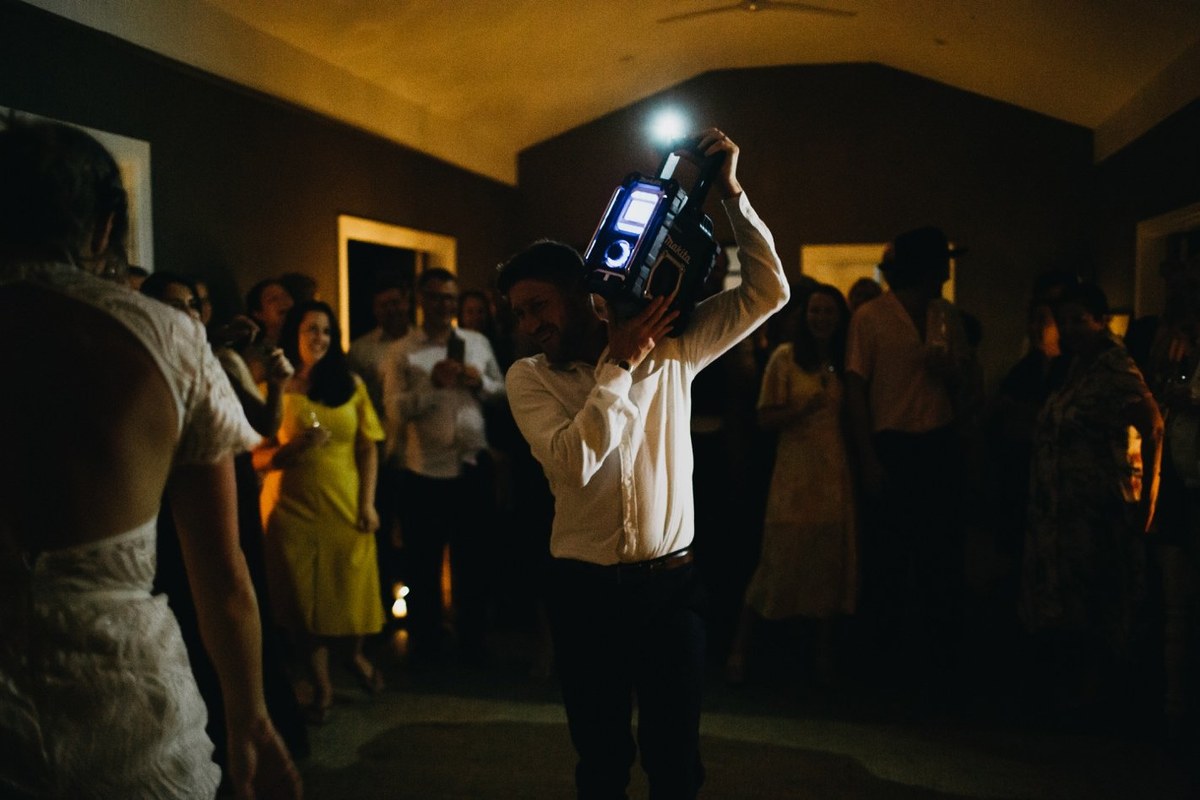 Guests gather around the dance floor as a man speaks in two moments. Photograph by documentary wedding photographer Joshua Mikhaiel.