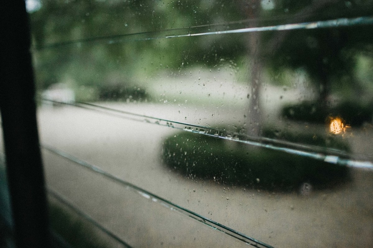 Rain falls across the garden as warm lights glow in the distance. Photograph by documentary wedding photographer Joshua Mikhaiel.
