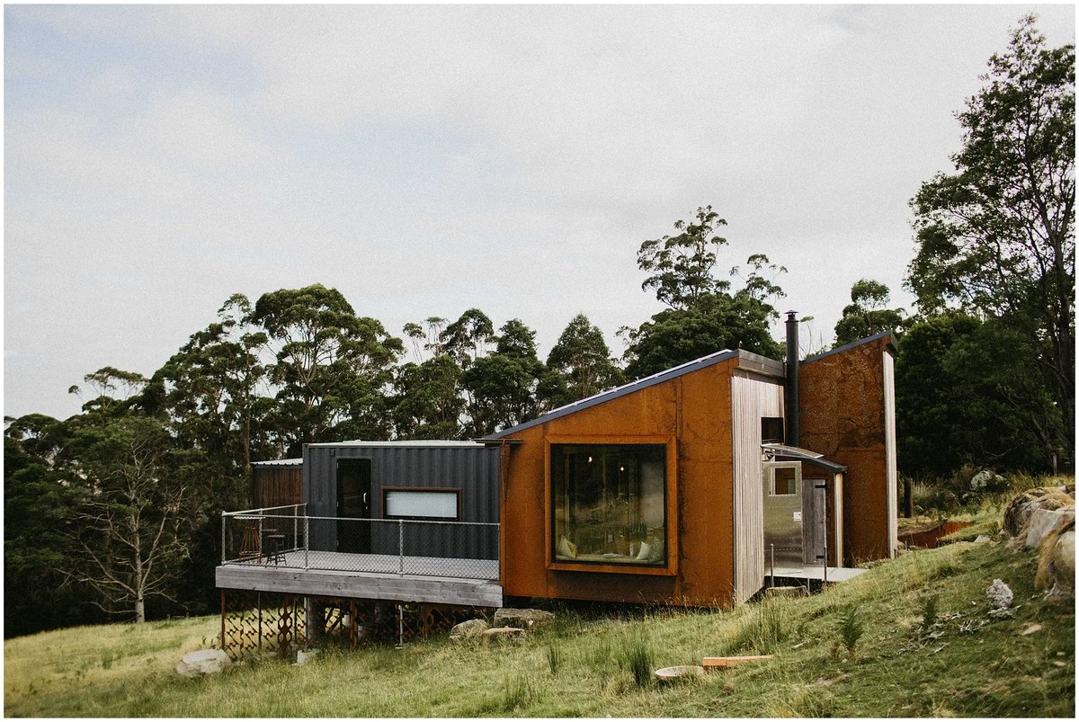 Timber cabin in the hills — Joshua Mikhaiel, documentary wedding photographer A contemporary timber cabin sits among trees on a green hillside. Photograph by documentary wedding photographer Joshua Mikhaiel.
