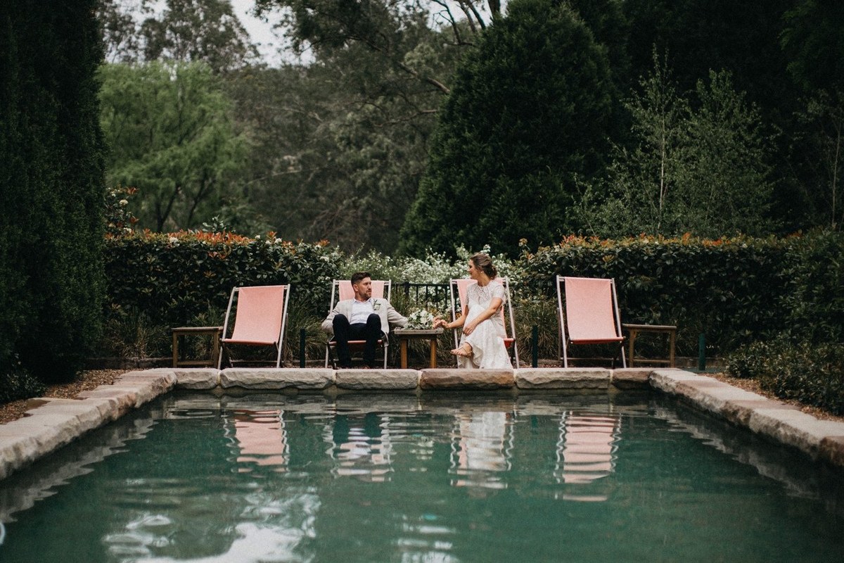 The bride and groom sit together beside the swimming pool. Photograph by documentary wedding photographer Joshua Mikhaiel.