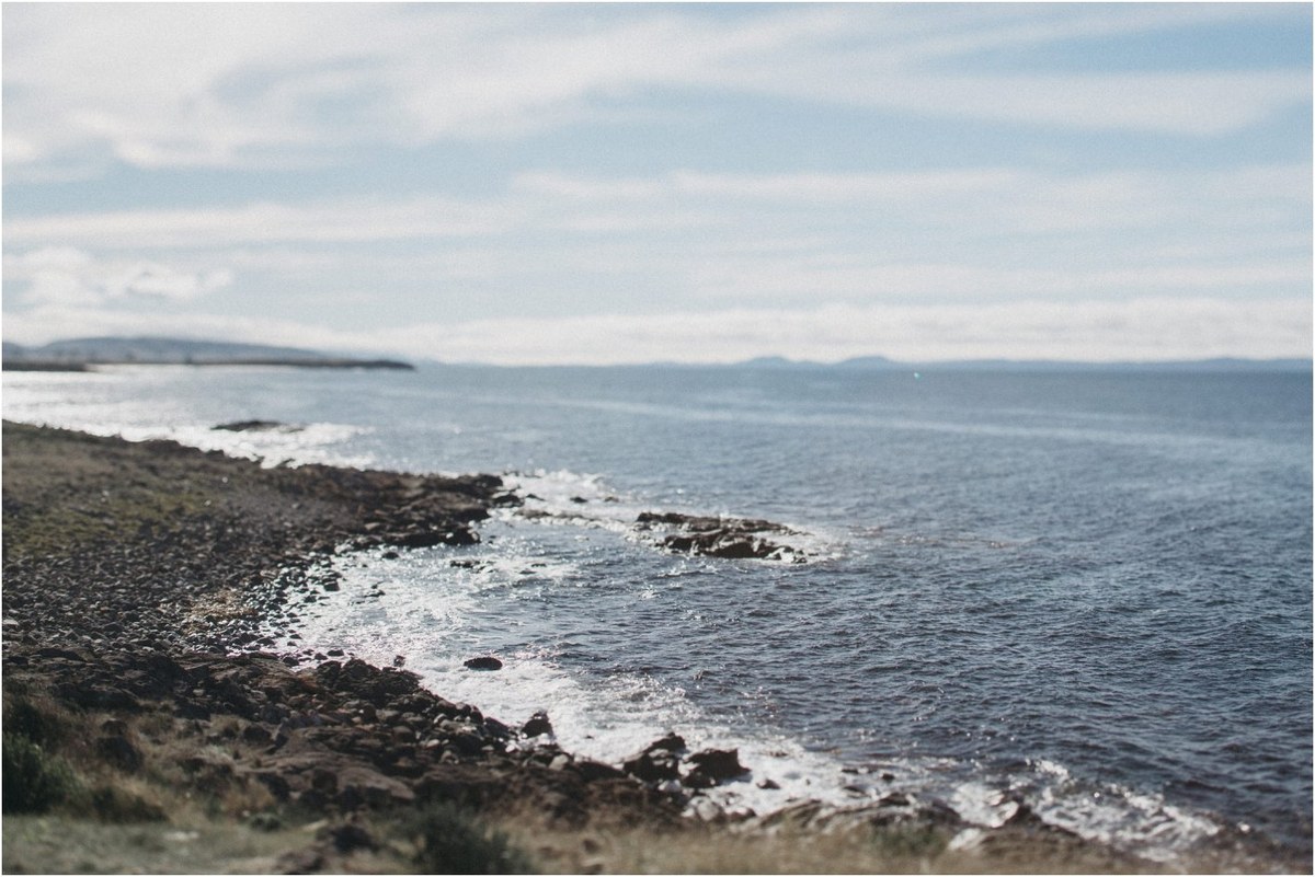 A wide view shows the rocky coastline and ocean at Thalia Haven, Tasmania, photographed by documentary wedding photographer Joshua Mikhaiel.