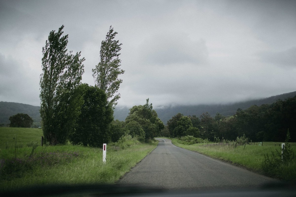 A country road runs between fields and trees beneath the cloudy sky. Photograph by documentary wedding photographer Joshua Mikhaiel.