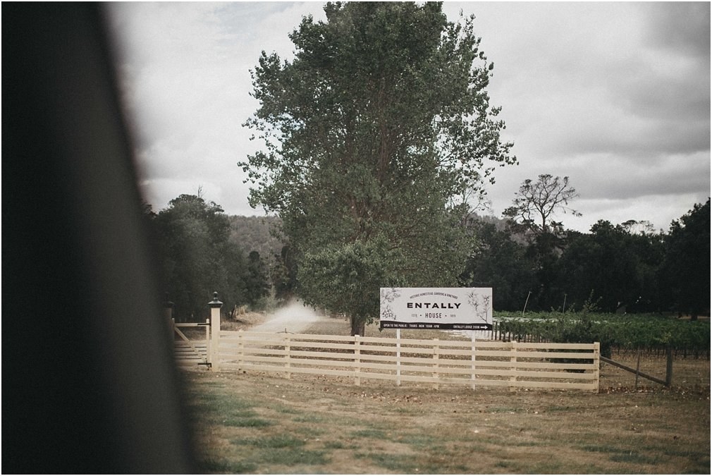A sign for Entally Lodge stands beside a white fence and large trees, photographed by documentary wedding photographer Joshua Mikhaiel.