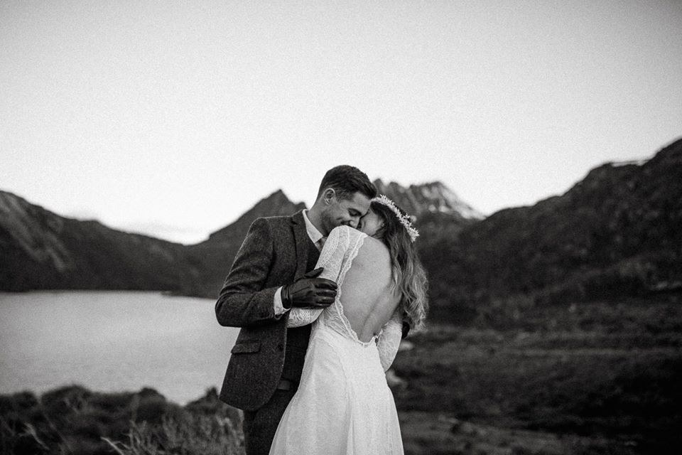 A couple embrace on a rocky ridge with mountains behind them, photographed in black and white by documentary wedding photographer Joshua Mikhaiel.