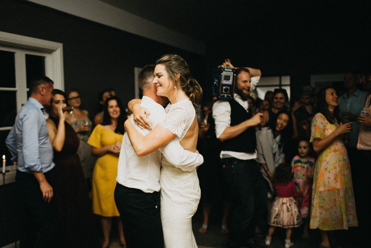 Guests dance around the bride and groom in the warmly lit room. Photograph by documentary wedding photographer Joshua Mikhaiel.