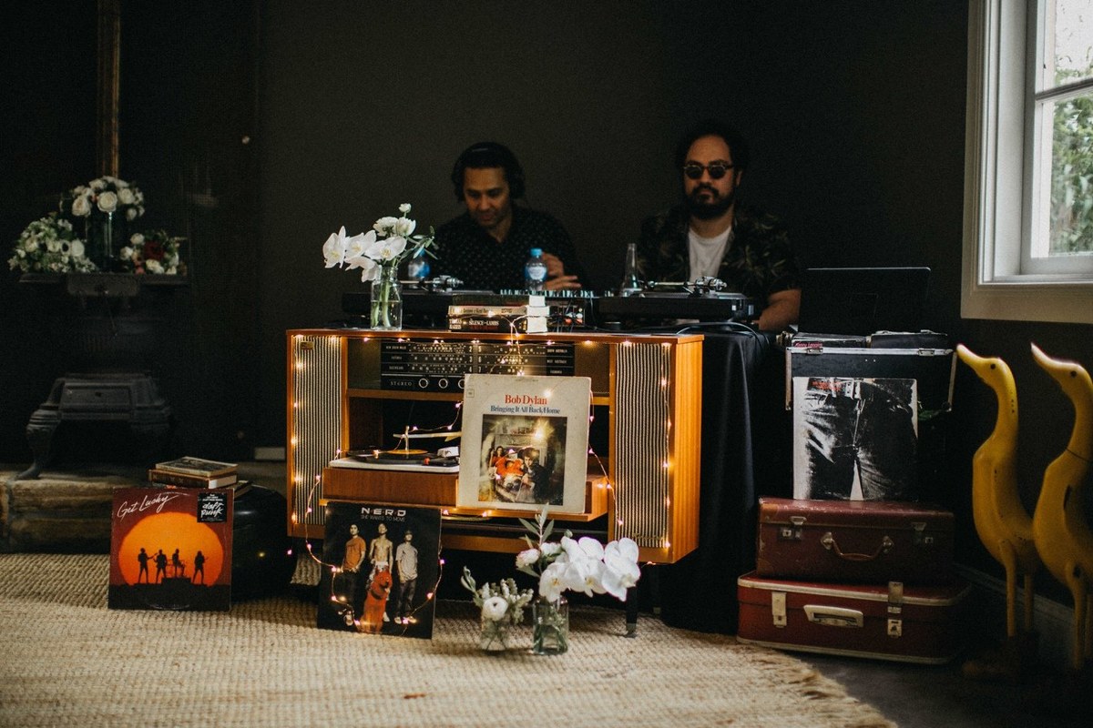 A DJ stands behind a decorated booth in the reception room. Photograph by documentary wedding photographer Joshua Mikhaiel.