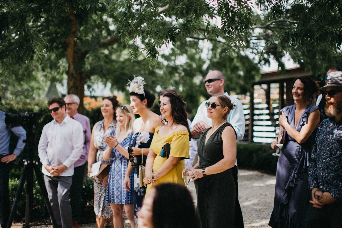 Guests sit in rows beneath the garden trees. Photograph by documentary wedding photographer Joshua Mikhaiel.