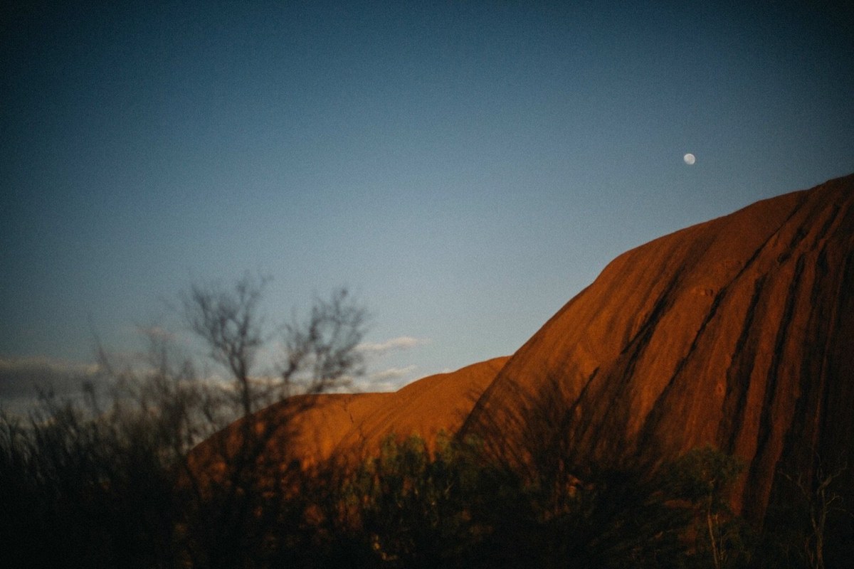 Uluru rises above the desert grass in the evening light, photographed by documentary wedding photographer Joshua Mikhaiel.