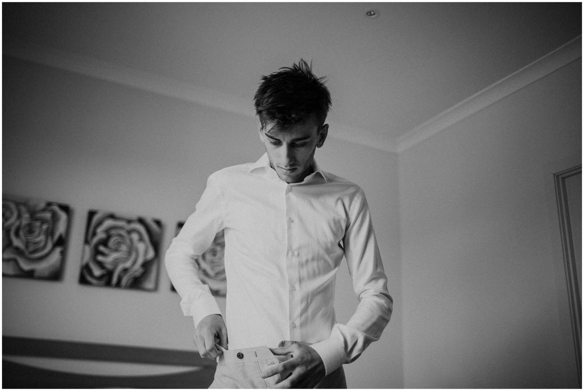 The groom adjusts his shirt while getting ready, photographed in black and white by documentary wedding photographer Joshua Mikhaiel.