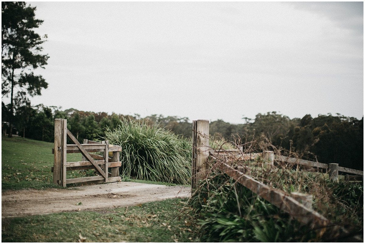A rural entrance gate opens to a tree-lined track. Photograph by documentary wedding photographer Joshua Mikhaiel.