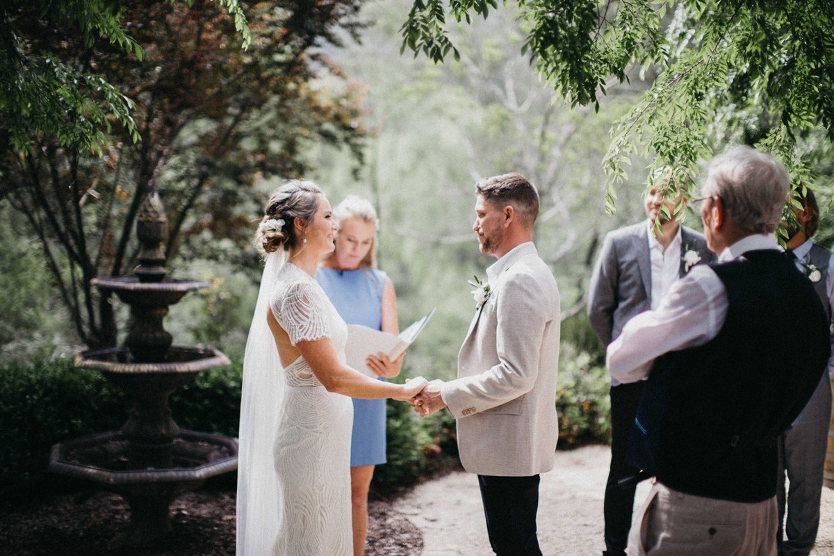 The bride holds hands with an older man beneath the garden trees. Photograph by documentary wedding photographer Joshua Mikhaiel.