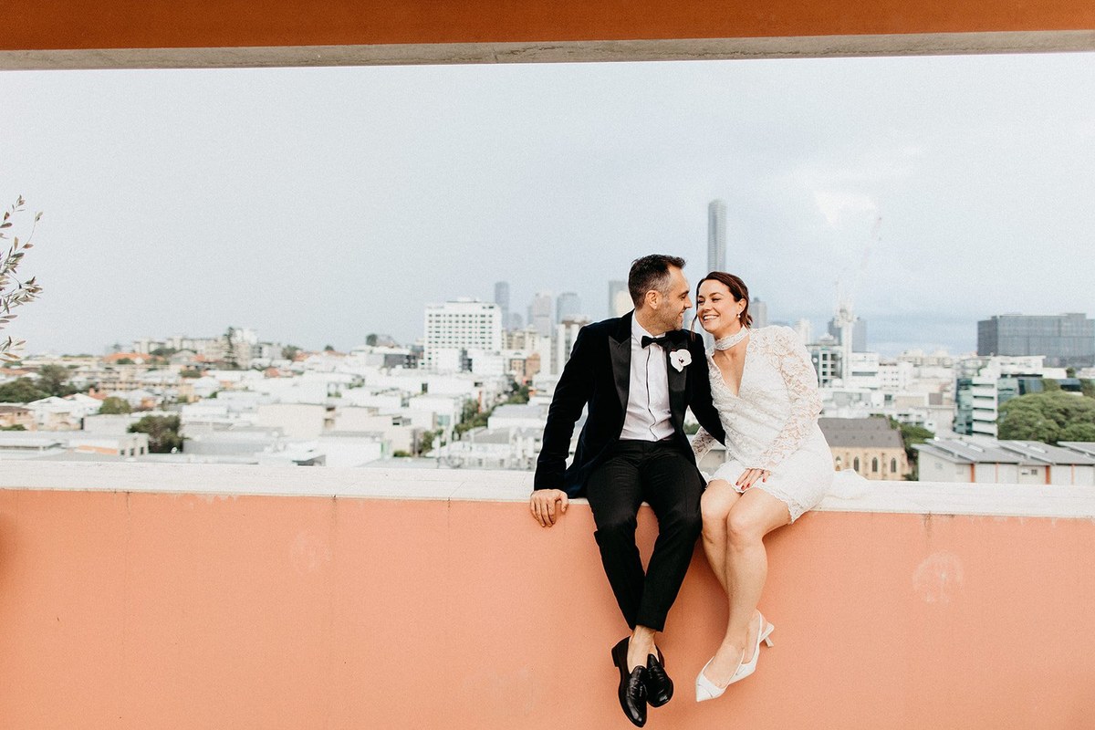 A couple sit together on a peach-colored balcony overlooking the city. Photograph by documentary wedding photographer Joshua Mikhaiel.