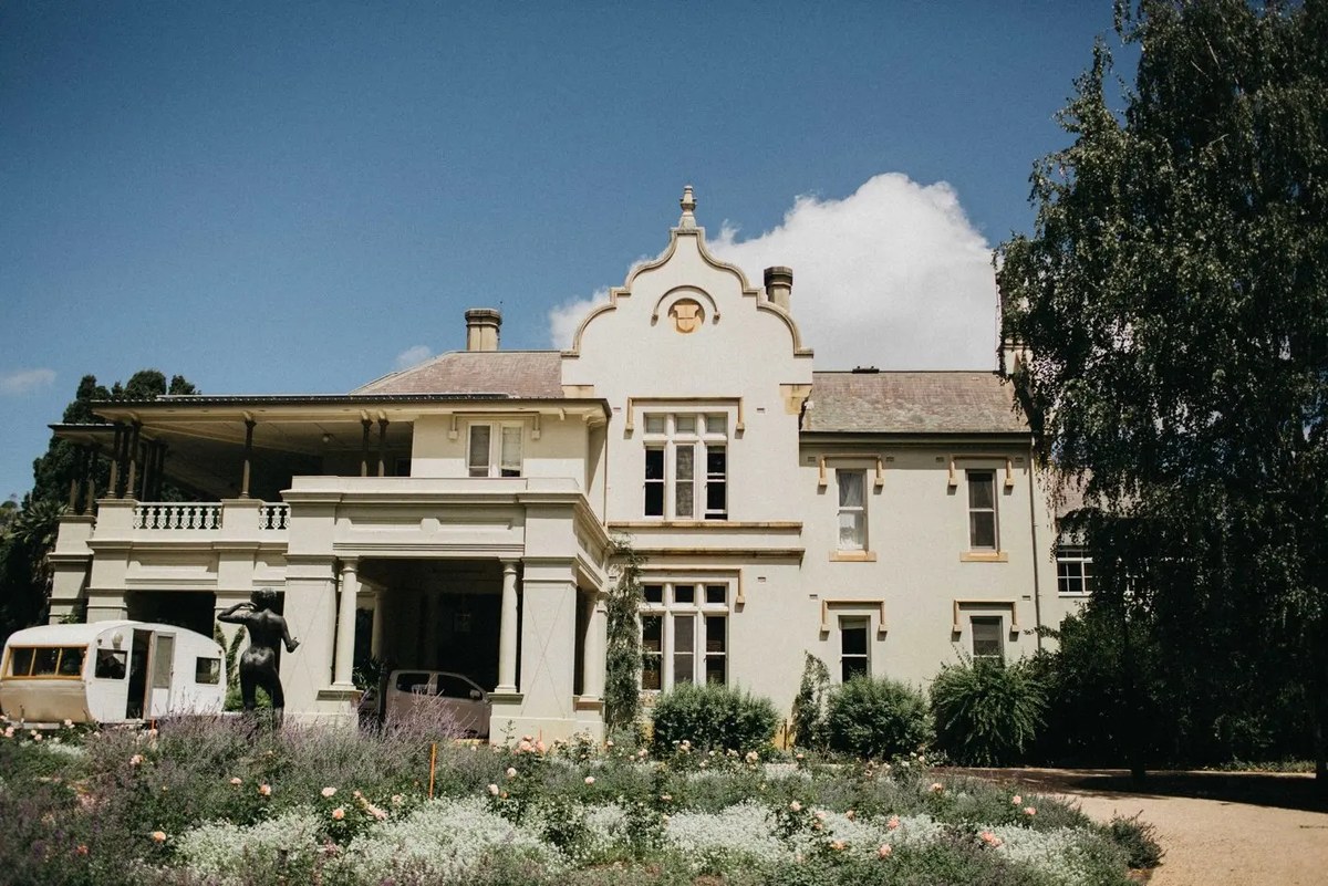 A large country estate stands behind a garden and broad lawn. Photograph by documentary wedding photographer Joshua Mikhaiel.