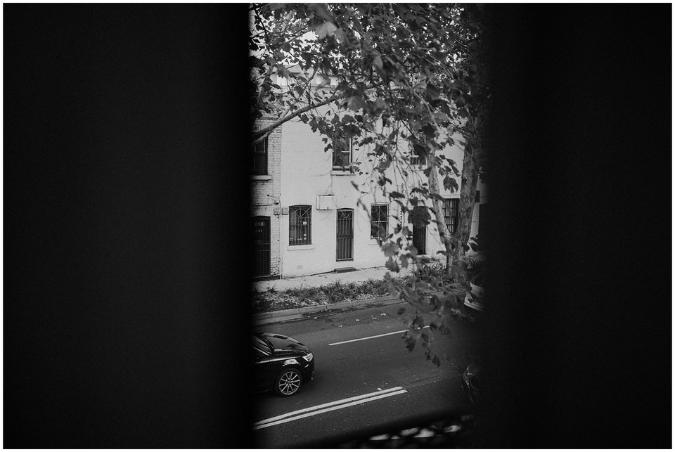 A black-and-white view looks through an archway toward a couple standing outside. Photograph by documentary wedding photographer Joshua Mikhaiel.