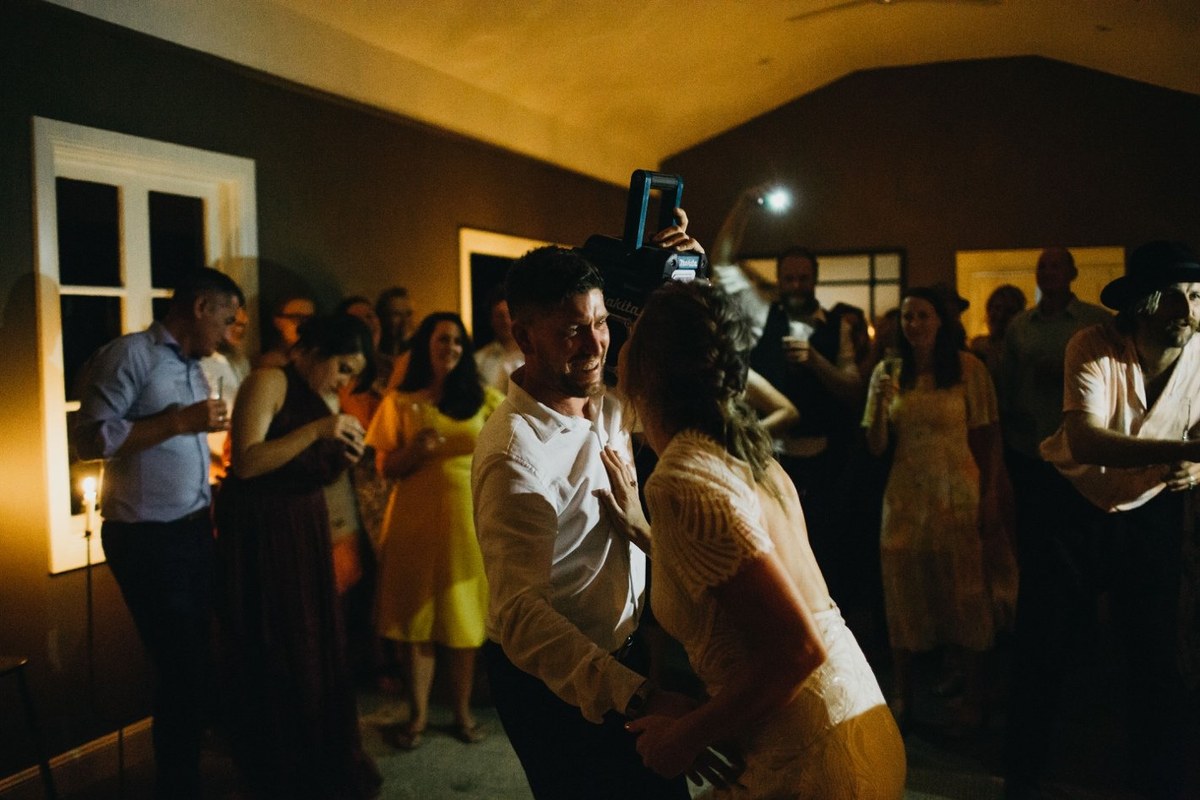 A man holds a wooden bar while another guest ducks beneath it. Photograph by documentary wedding photographer Joshua Mikhaiel.