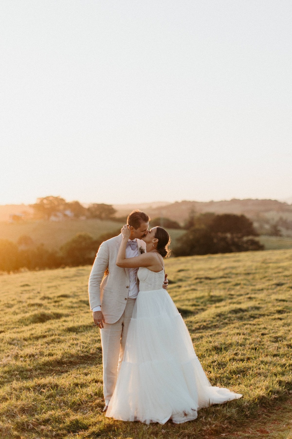 A couple embrace in a rolling paddock at sunset, photographed by documentary wedding photographer Joshua Mikhaiel.
